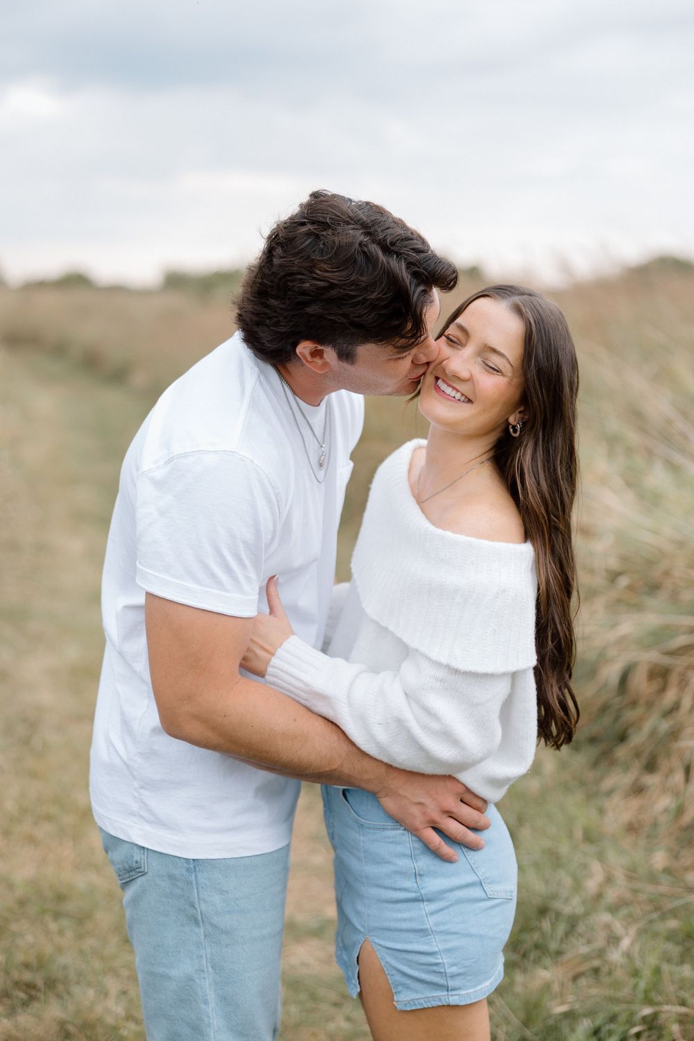 Romantic couple in matching white outfits embracing in grassy field.