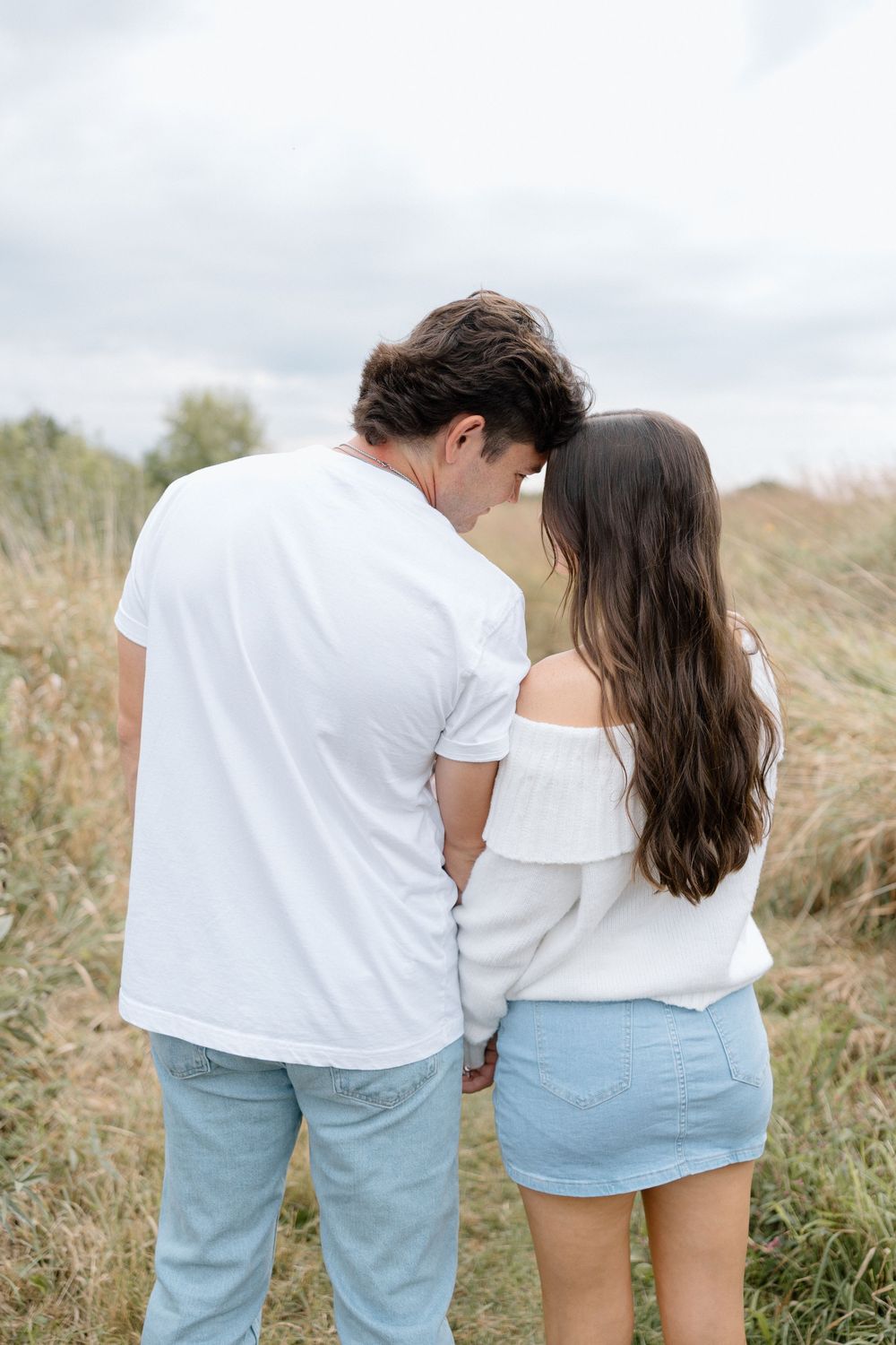 Couple wearing coordinated white tops and light denim sharing intimate moment outdoors.