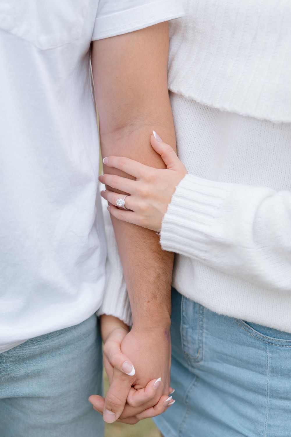 Close-up of couple holding hands wearing white tops and light denim.