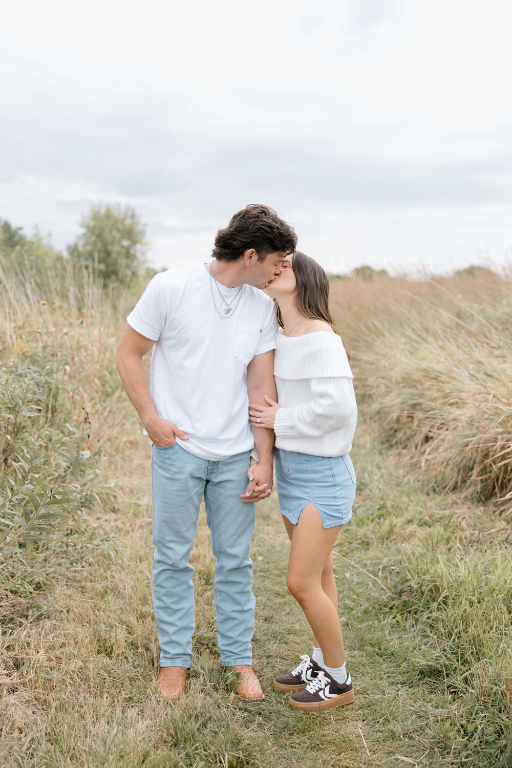 Couple in matching white and denim outfits walking together through tall grass.