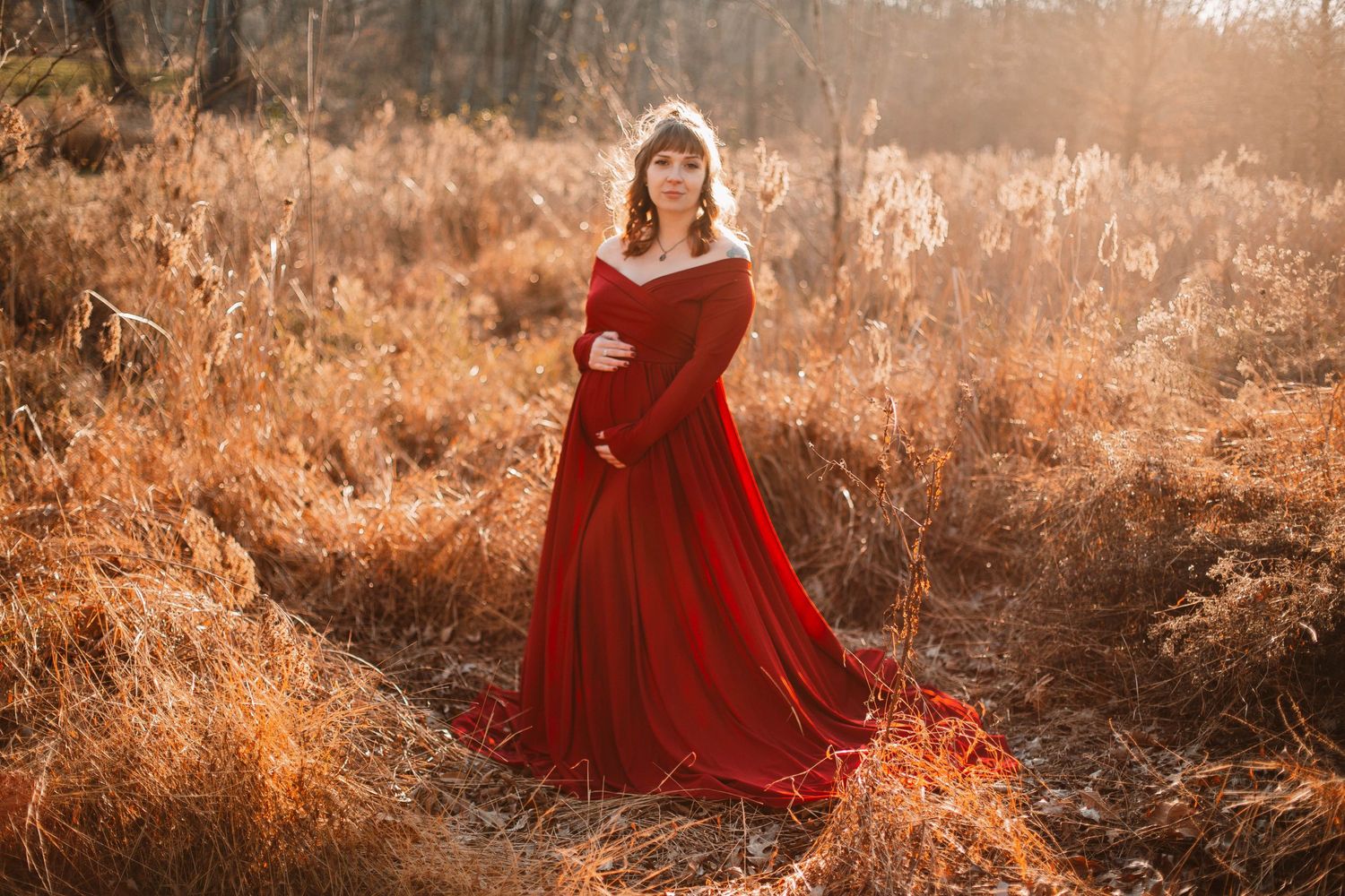 Person in flowing red dress poses dramatically in golden sunlit field.