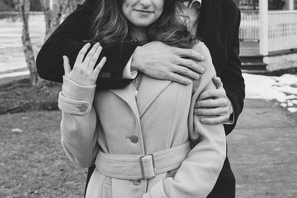 A couple embraces while standing outdoors on a winter day near a gazebo. Château des  Fleures Wedding Photographer