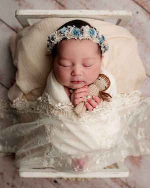 Sleeping newborn in white wrap wearing delicate blue floral crown.