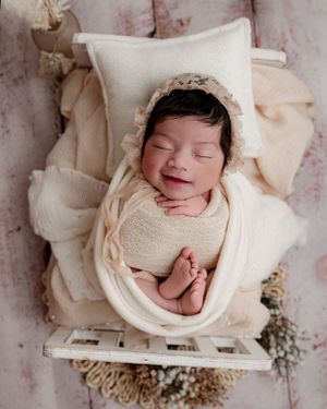 Peaceful newborn sleeping in white swaddle wrap on vintage white crate with soft textured backdrop.