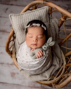 Newborn portrait in woven chair with gray knit blanket and soft white wrap.
