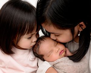 Sweet moment of siblings giving sleeping newborn gentle kisses during photo session.