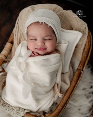 Smiling newborn wrapped in white swaddle poses in vintage wicker basket.