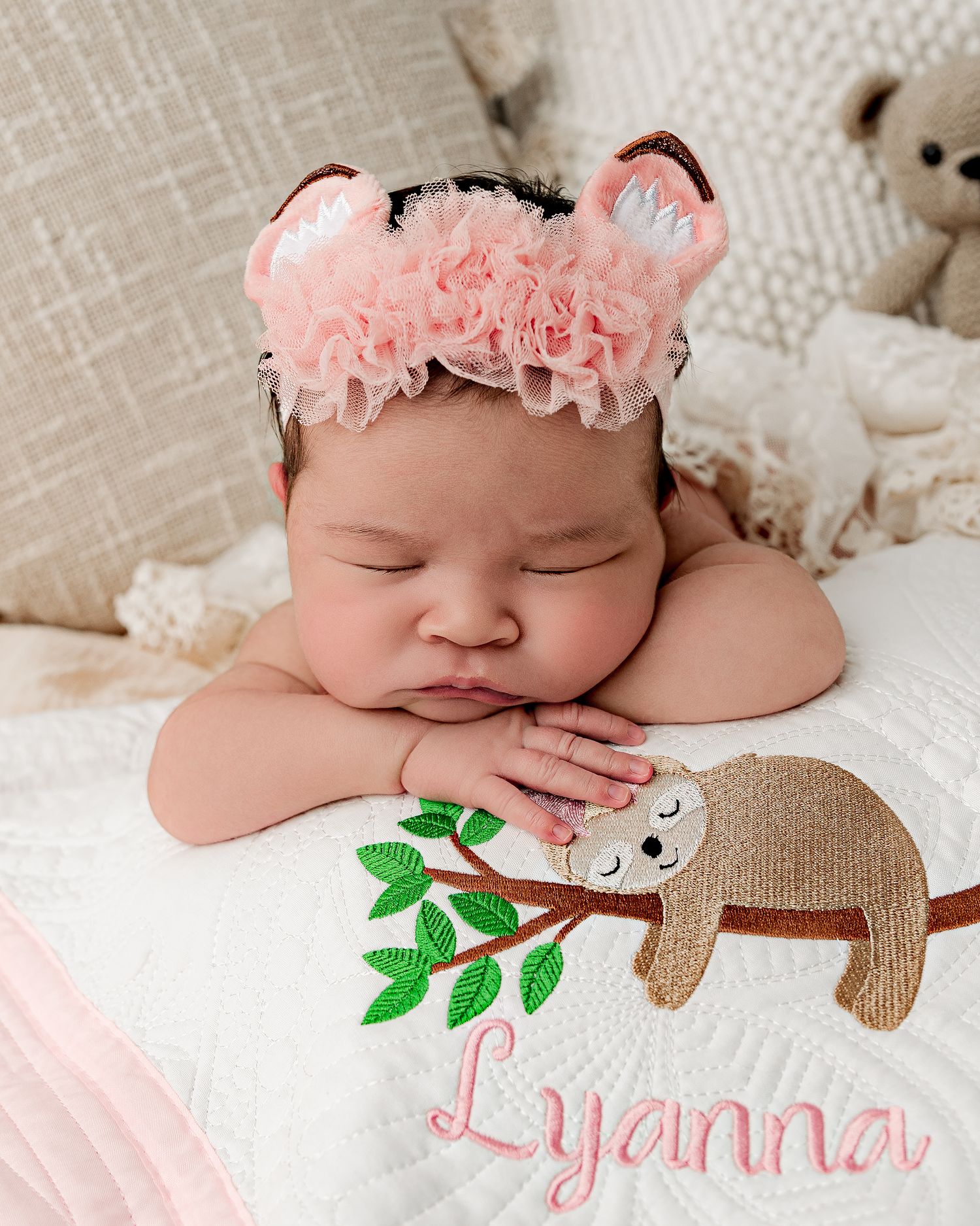 Sleeping newborn wearing pink animal headband with embroidered sloth blanket.