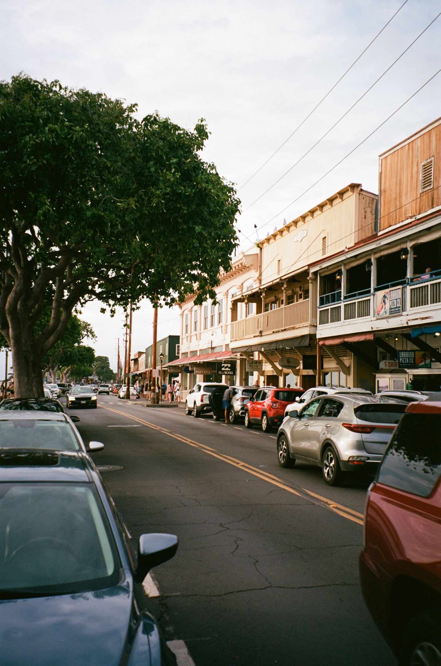 A small town main street with parked cars and historic buildings lined with trees.