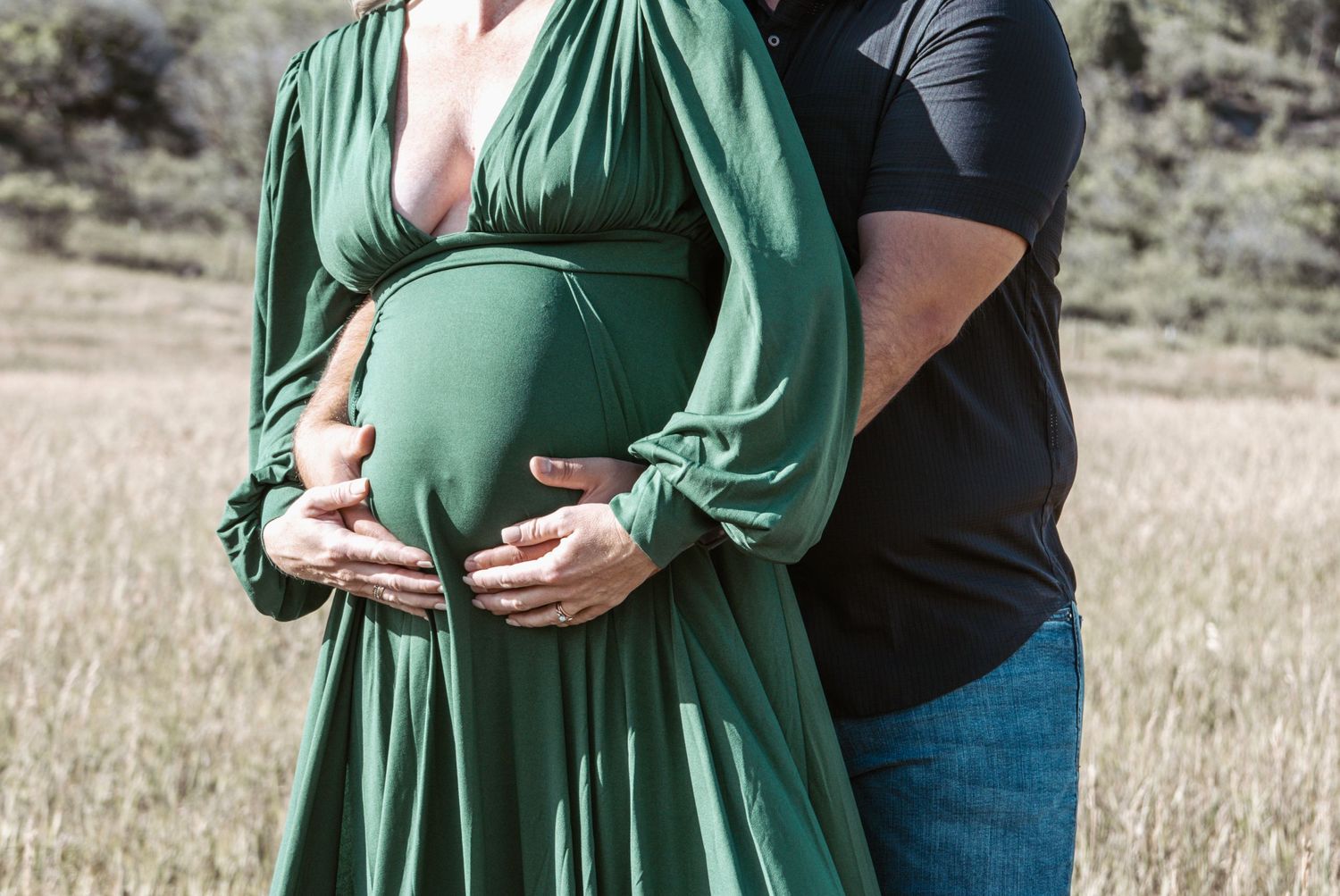 Maternity photo showing couple's hands on pregnant belly in emerald green dress.