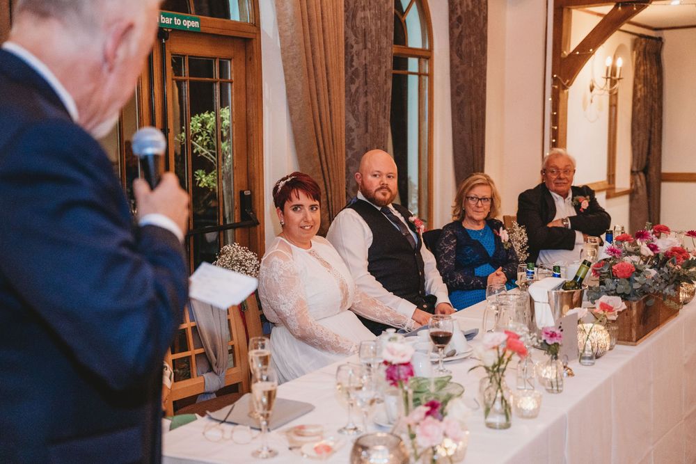 Elegant wedding reception dinner with guests seated at long tables decorated with floral arrangements.