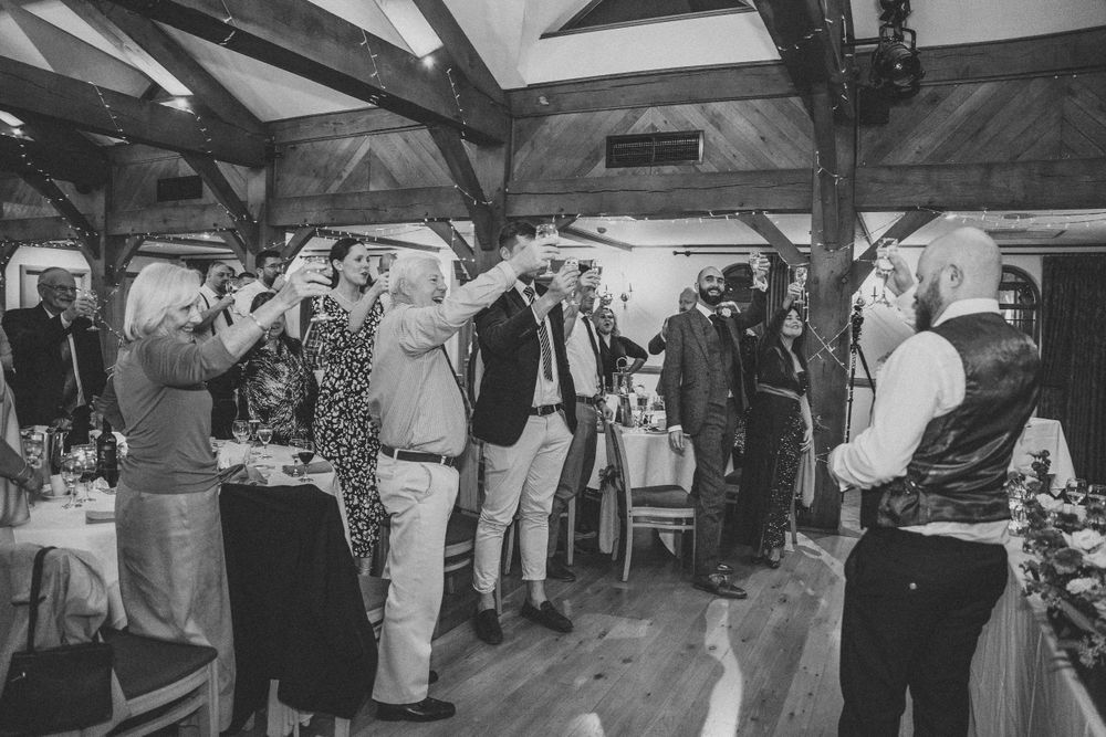 Black and white photo of wedding guests dancing together on a wooden dance floor.