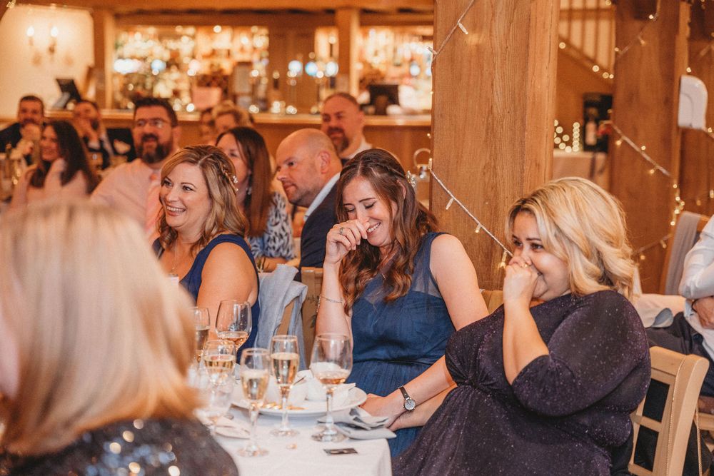 Wedding guests enjoy a lively reception celebration in an elegant indoor venue with wooden beams and warm lighting.