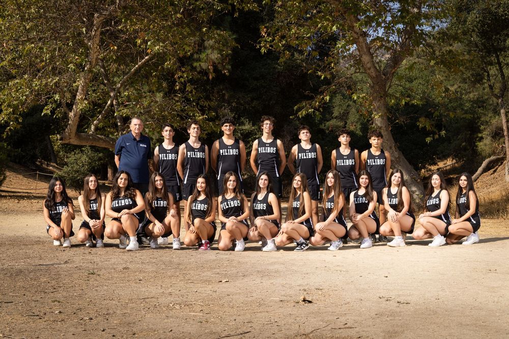 A group of athletes in matching uniforms sit together on a beach during a team photoshoot.