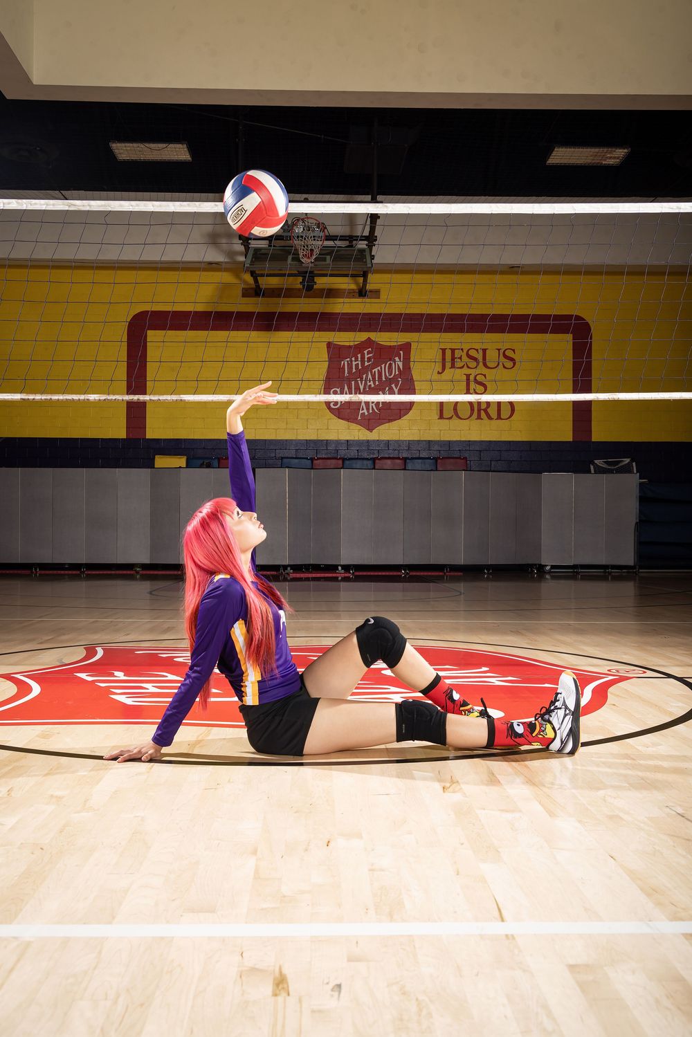 A volleyball player dives across a gym floor to save a ball during a game at an indoor court with red markings.