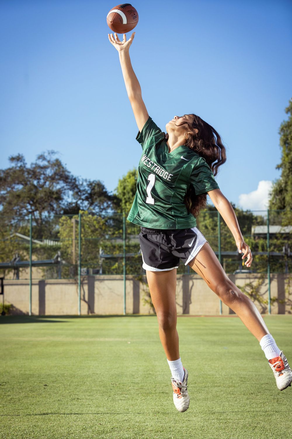 Football player in green jersey kicking ball in sequence motion capture on sunny grass field.