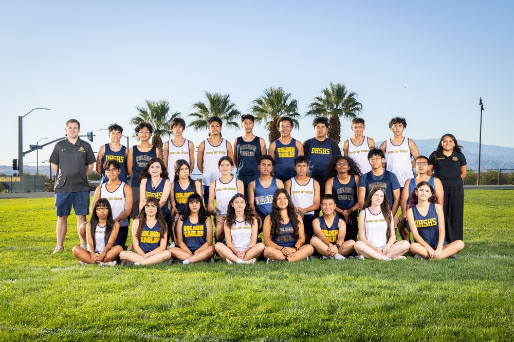 A group of students sits together on a grassy hillside for a casual outdoor photo session.