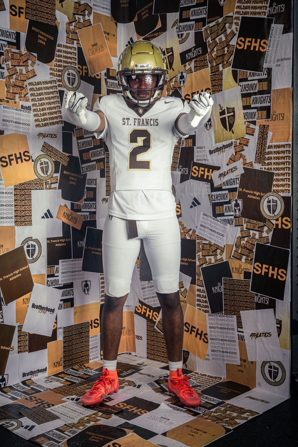 St. Francis Knights football player wearing white number 2 jersey and helmet poses in front of SFHS branded backdrop.