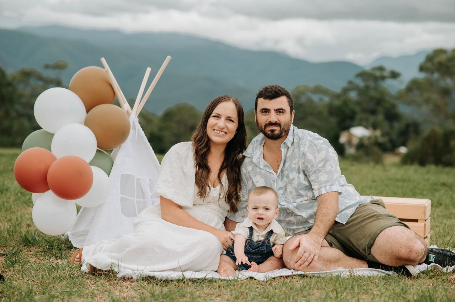 Family celebrating baby's first birthday with teepee tent setup in mountain backdrop.