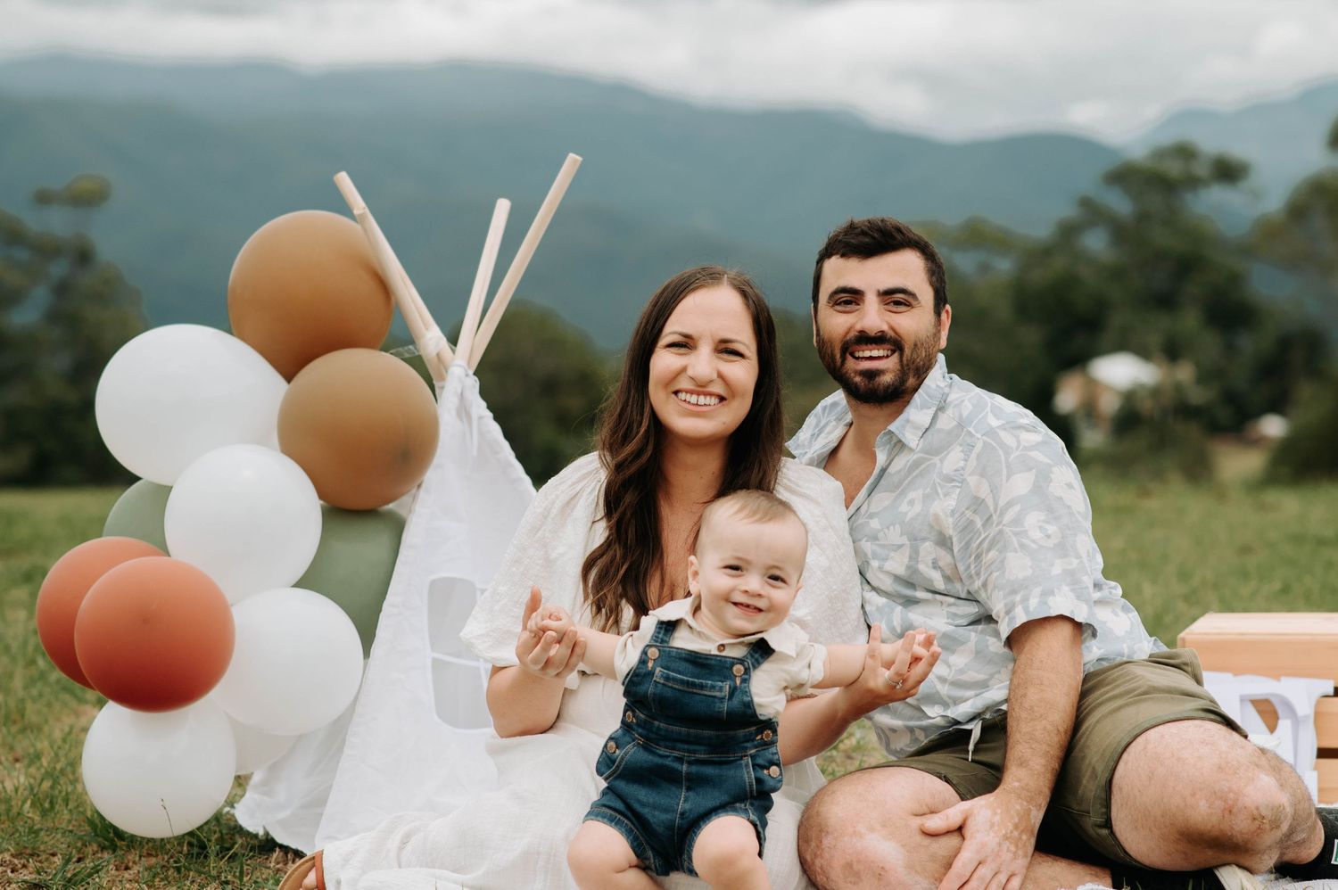 Joyful family moment during baby's first birthday photoshoot with teepee and balloons.