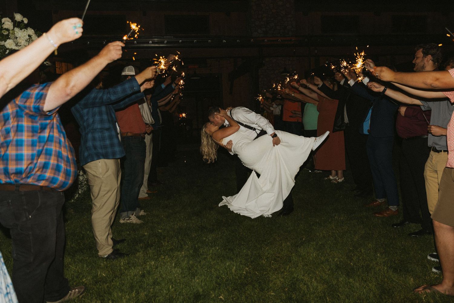 Wedding reception guests dancing outdoors at night with string lights.