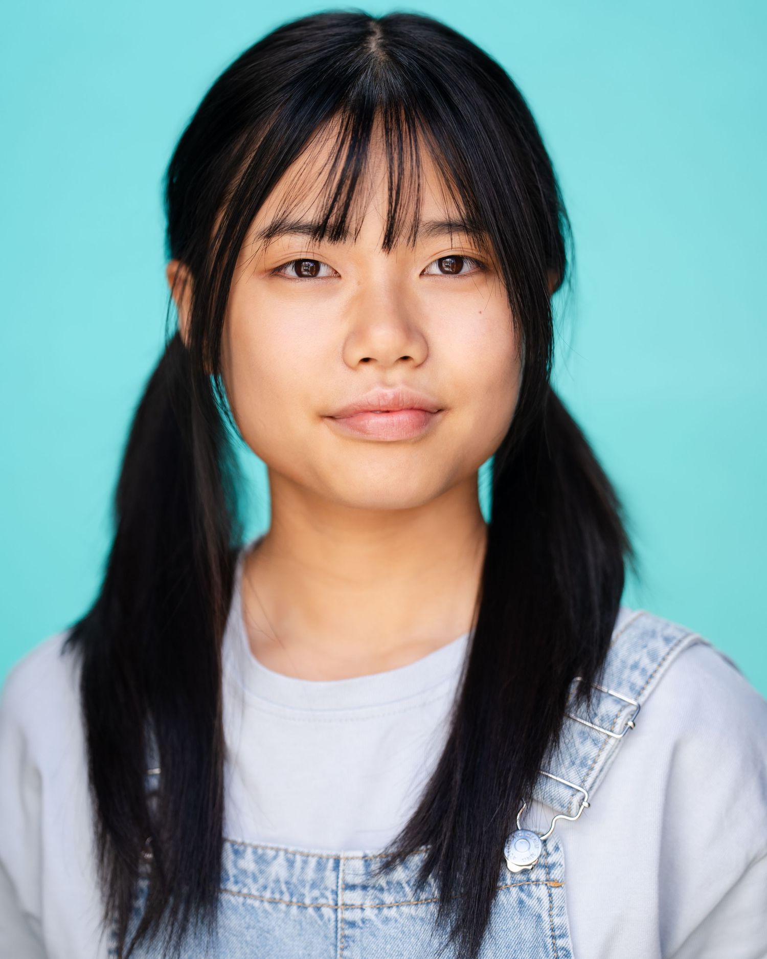 Portrait of smiling person in denim overalls with blue bow headband and pigtails in Guildford, Surrey.