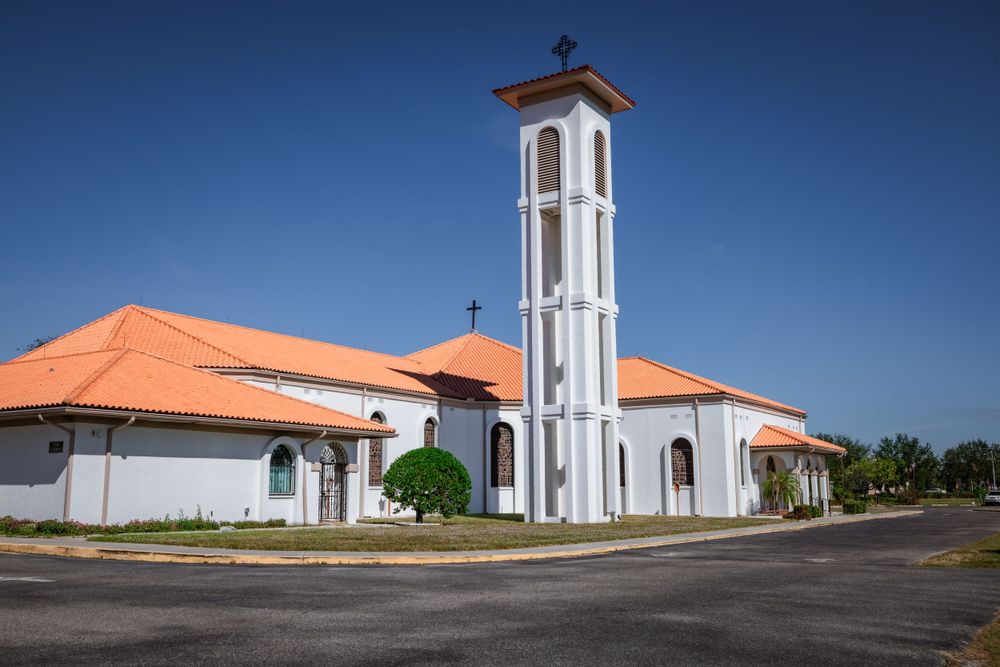 Modern white church building with tall bell tower and orange terra cotta roof situated on corner lot.