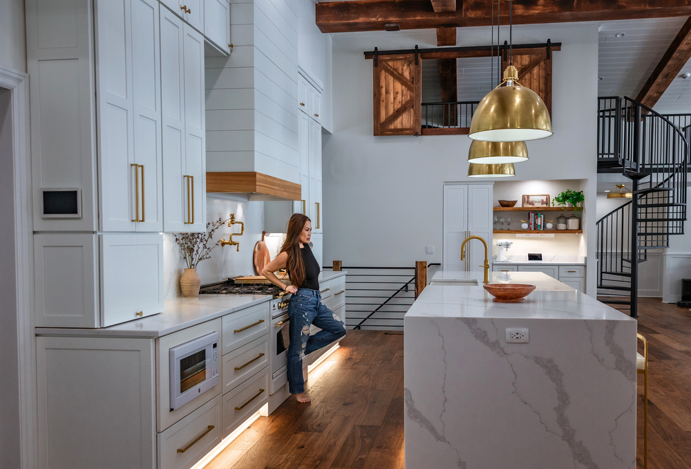 Modern open concept kitchen and living area with white walls, wooden beams, and natural light streaming through windows.