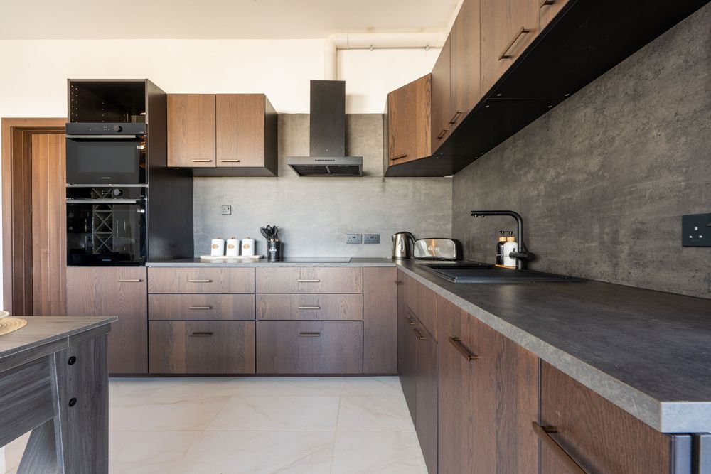 Modern L-shaped kitchen with wooden cabinets, black countertops, and stainless steel appliances.