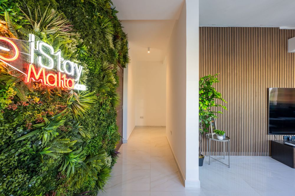 Living space with green wall garden and illuminated neon sign against wood paneled accent wall.