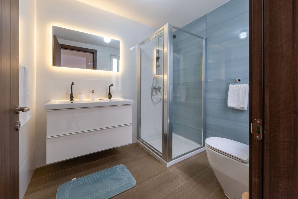 Modern bathroom featuring floating vanity, backlit mirror, and glass shower enclosure.