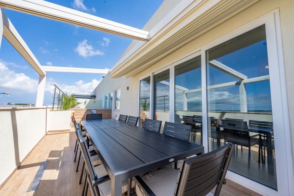 Outdoor terrace with sleek black furniture and glass railings against a bright blue sky.