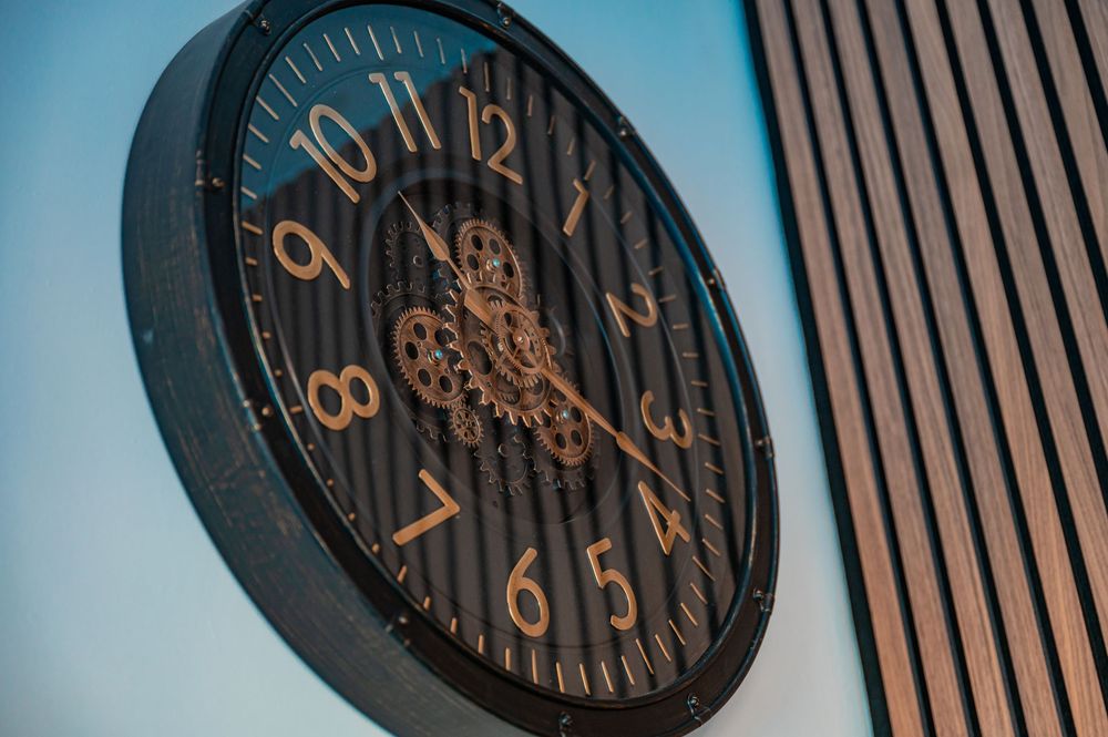 Large decorative wall clock with dark face and metallic numbers in modern setting.
