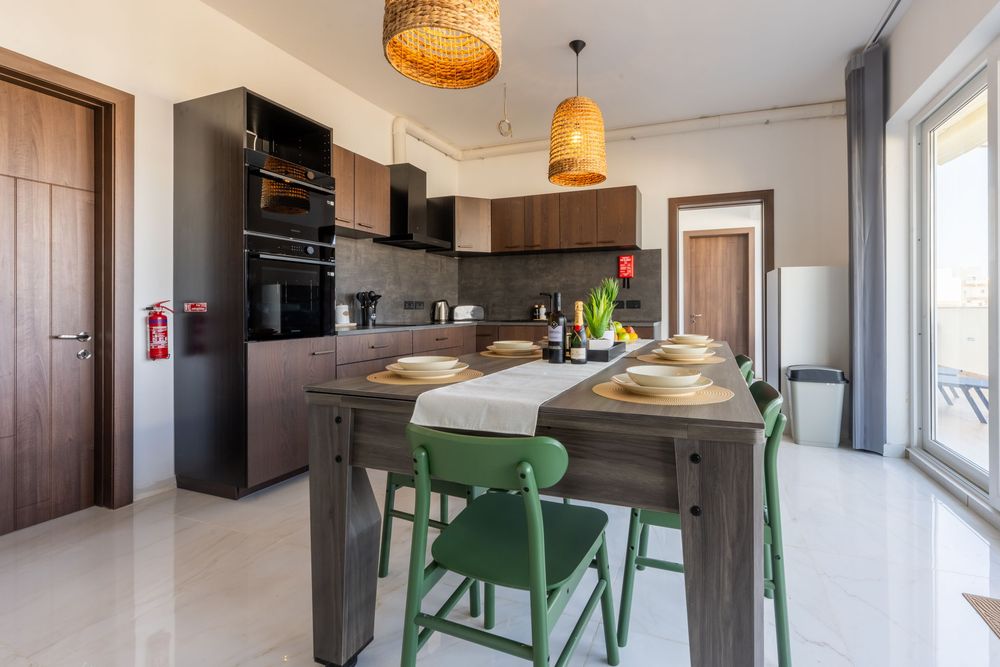 Contemporary kitchen dining area with green chairs and woven pendant lights above wooden table.