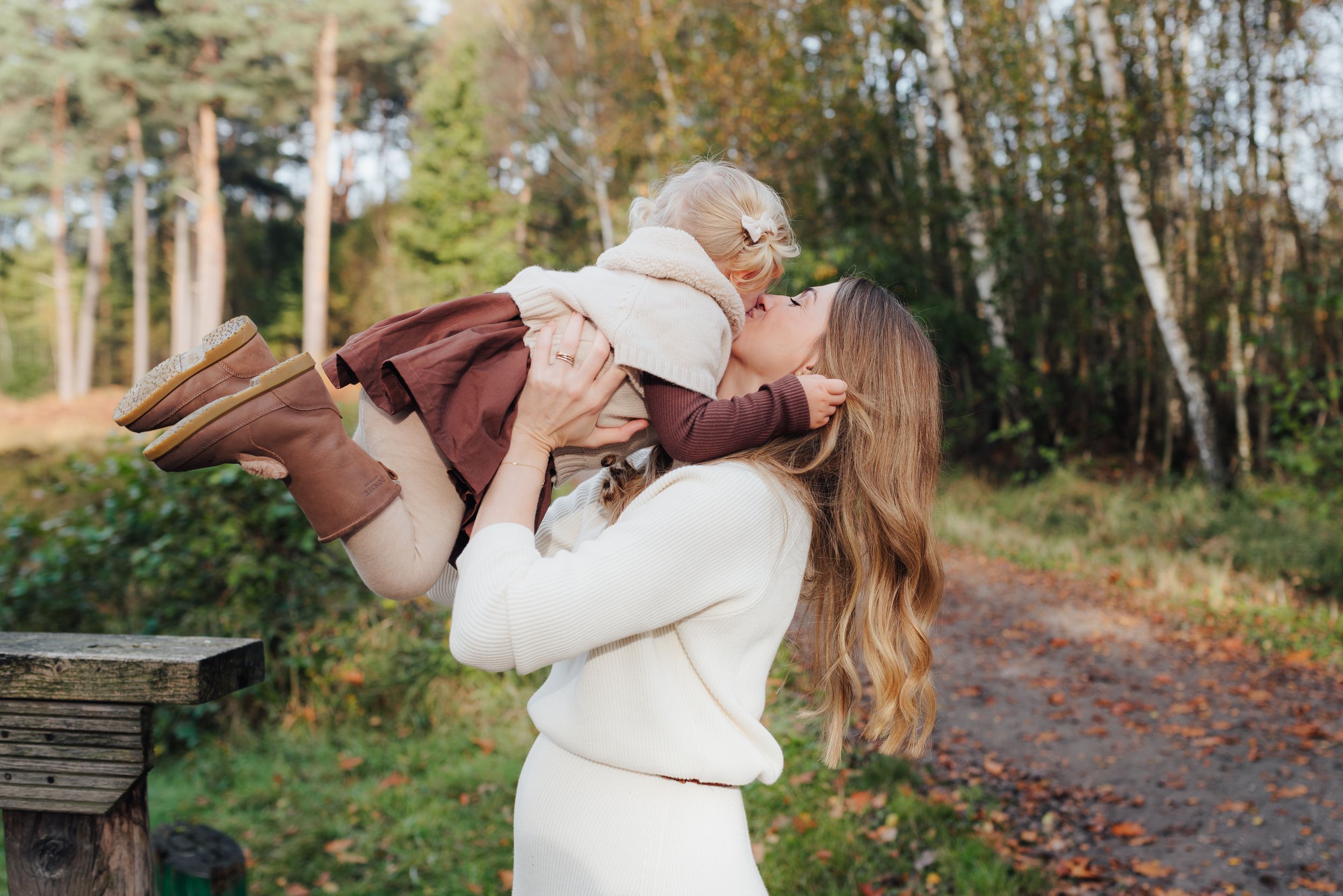 A tender moment between parent and child in white sweaters along an autumn forest path.