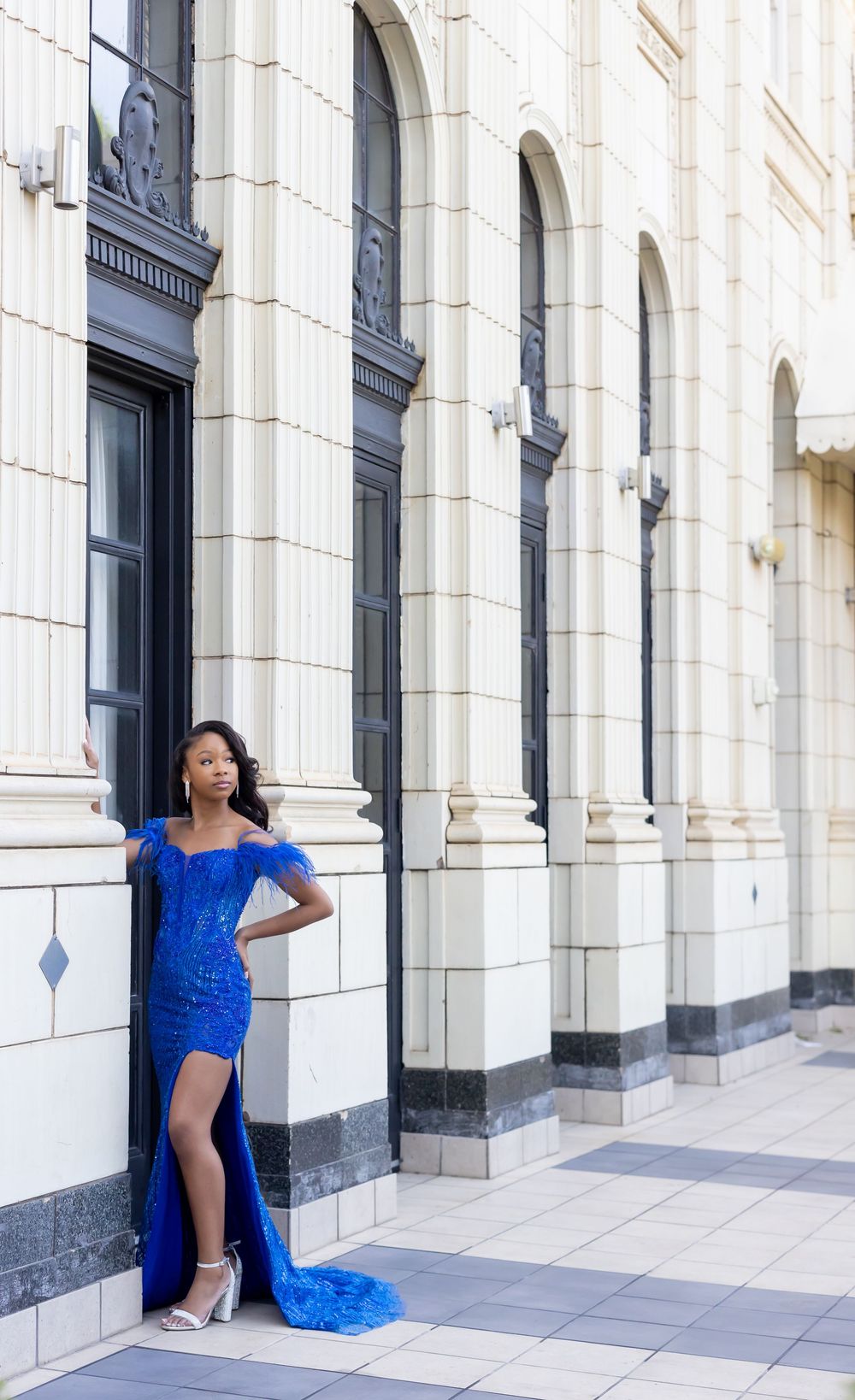 Prom portrait featuring stunning royal blue sequined gown with high slit poses elegantly against white classical building columns