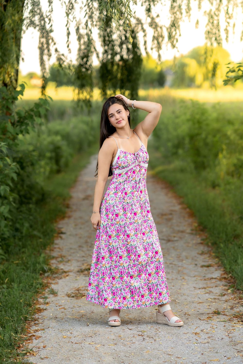 Romantic summer scene with colorful floral dress on dirt path under weeping willow branches at golden hour.