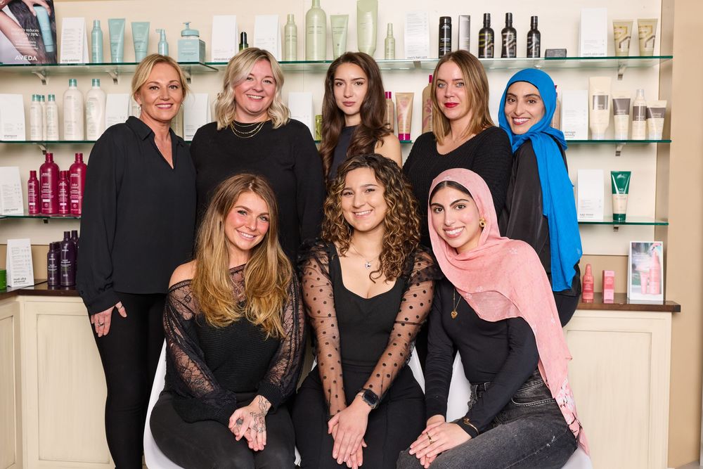 Group of salon staff members pose together in front of retail product display shelves.