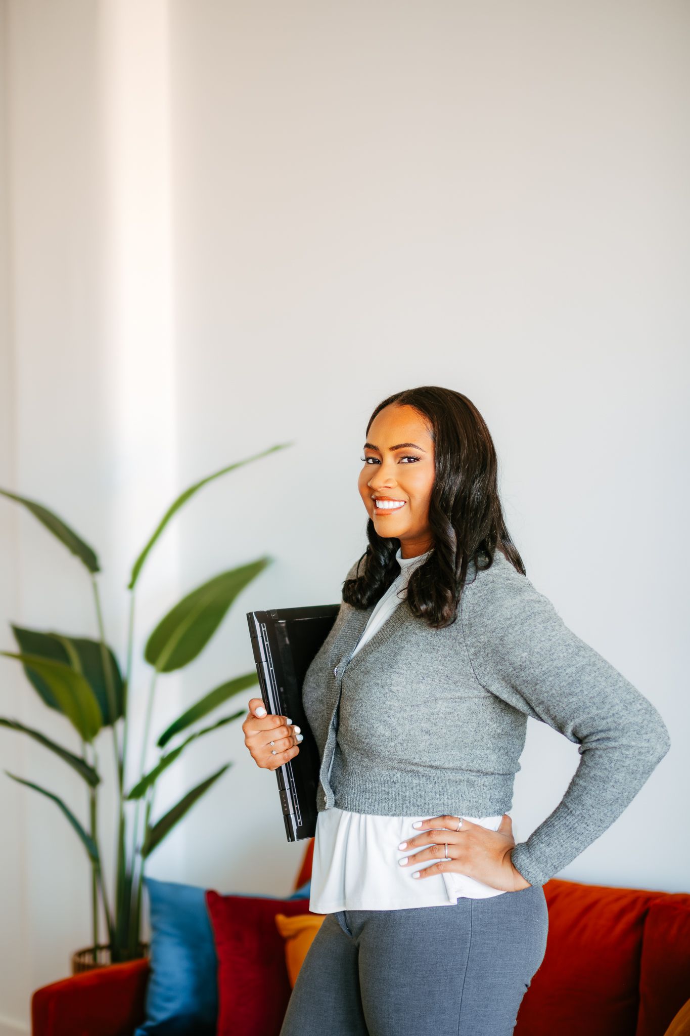 Business professional in grey sweater holding portfolio in modern office with red couch.