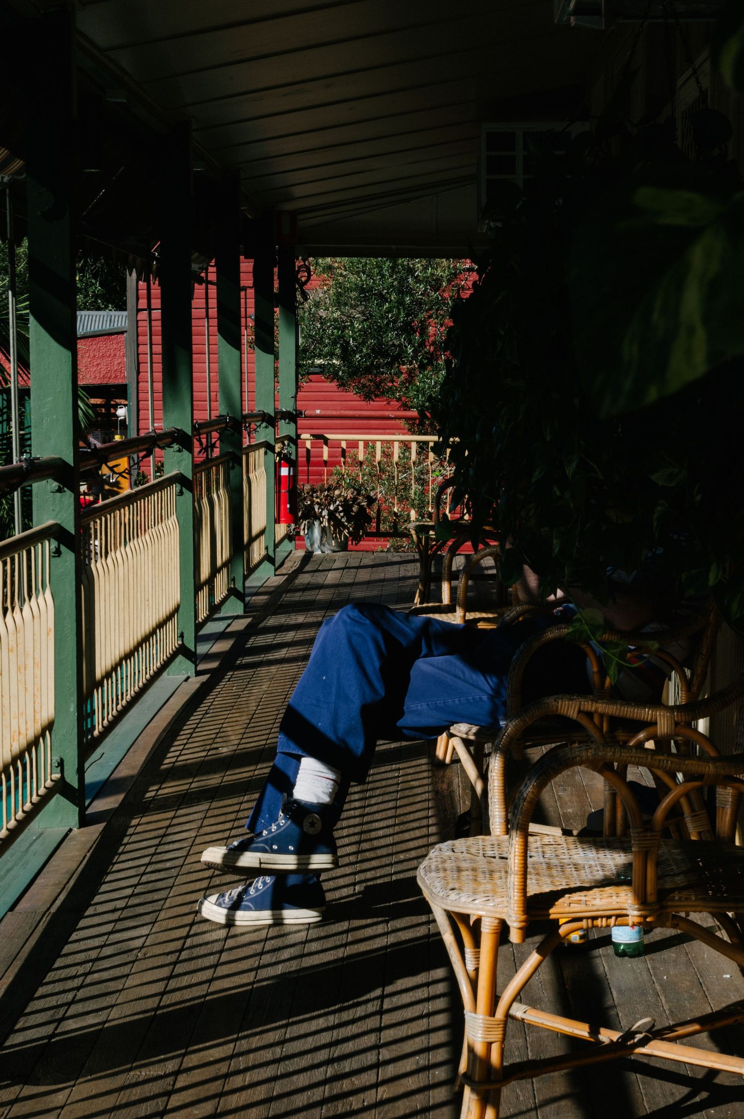 Long shadows cast dramatic patterns across a wooden deck where someone rests on patio furniture in blue clothing.