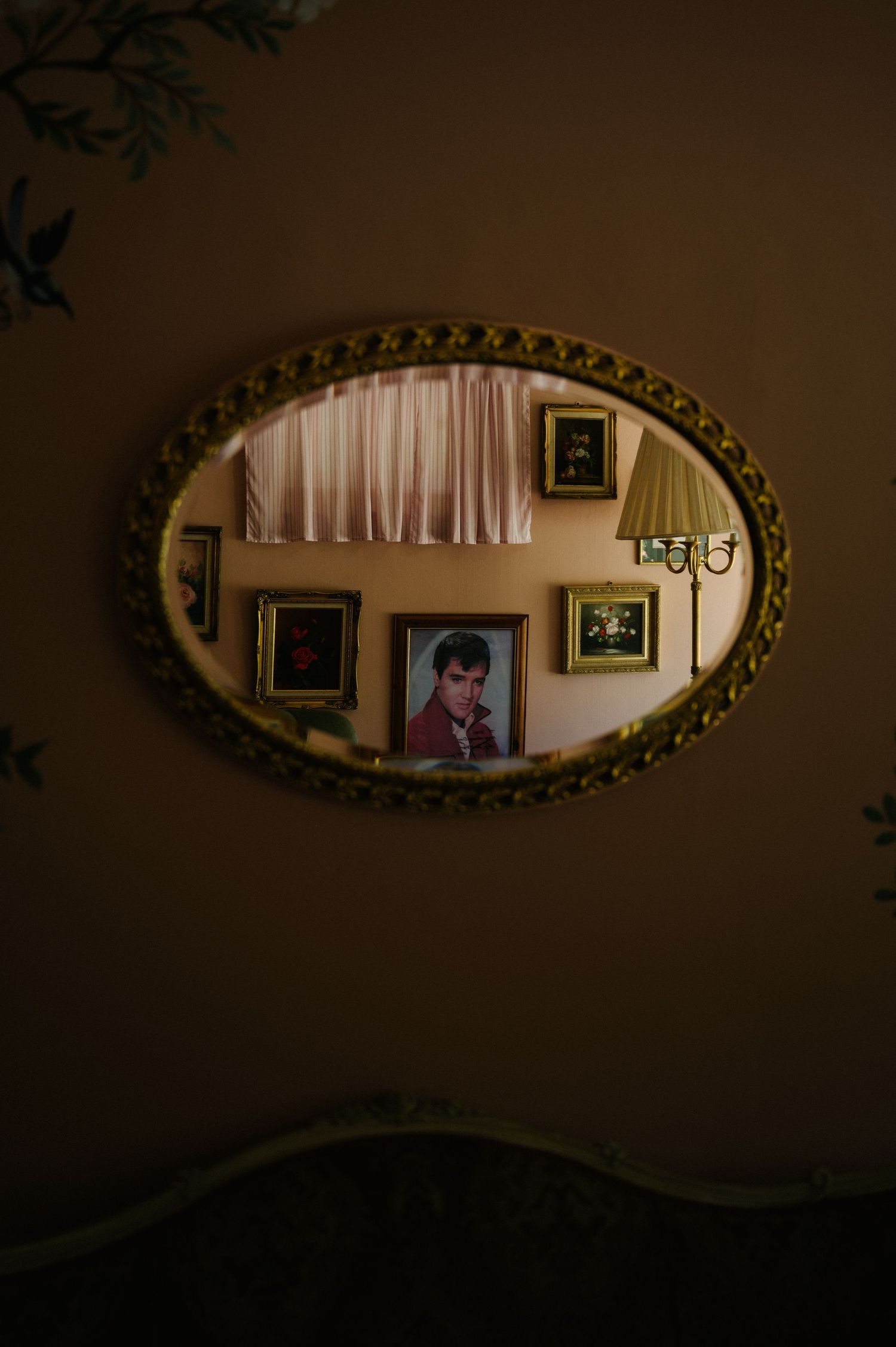 A sequence of oval ornate gold mirrors hanging on a dark wall reflects dim interior lighting and room decor.