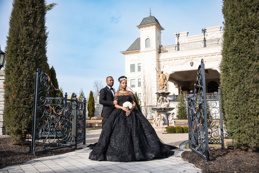 Bride in black dress with groom in front of The Legacy Castle gates