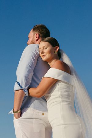 A series of photos showing a couple in white wedding attire embracing against a bright blue sky background.