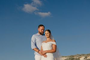 A couple embraces on a beach cliff during sunset with the ocean and sky creating a romantic backdrop.
