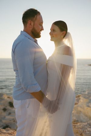 A couple shares an intimate moment on the beach at sunset with a flowing white veil creating a romantic silhouette.
