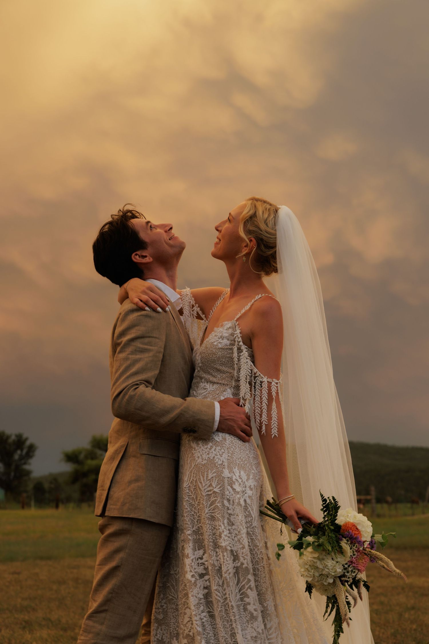 Bride and Groom embrace and stare at the dramatic cloudy sky.