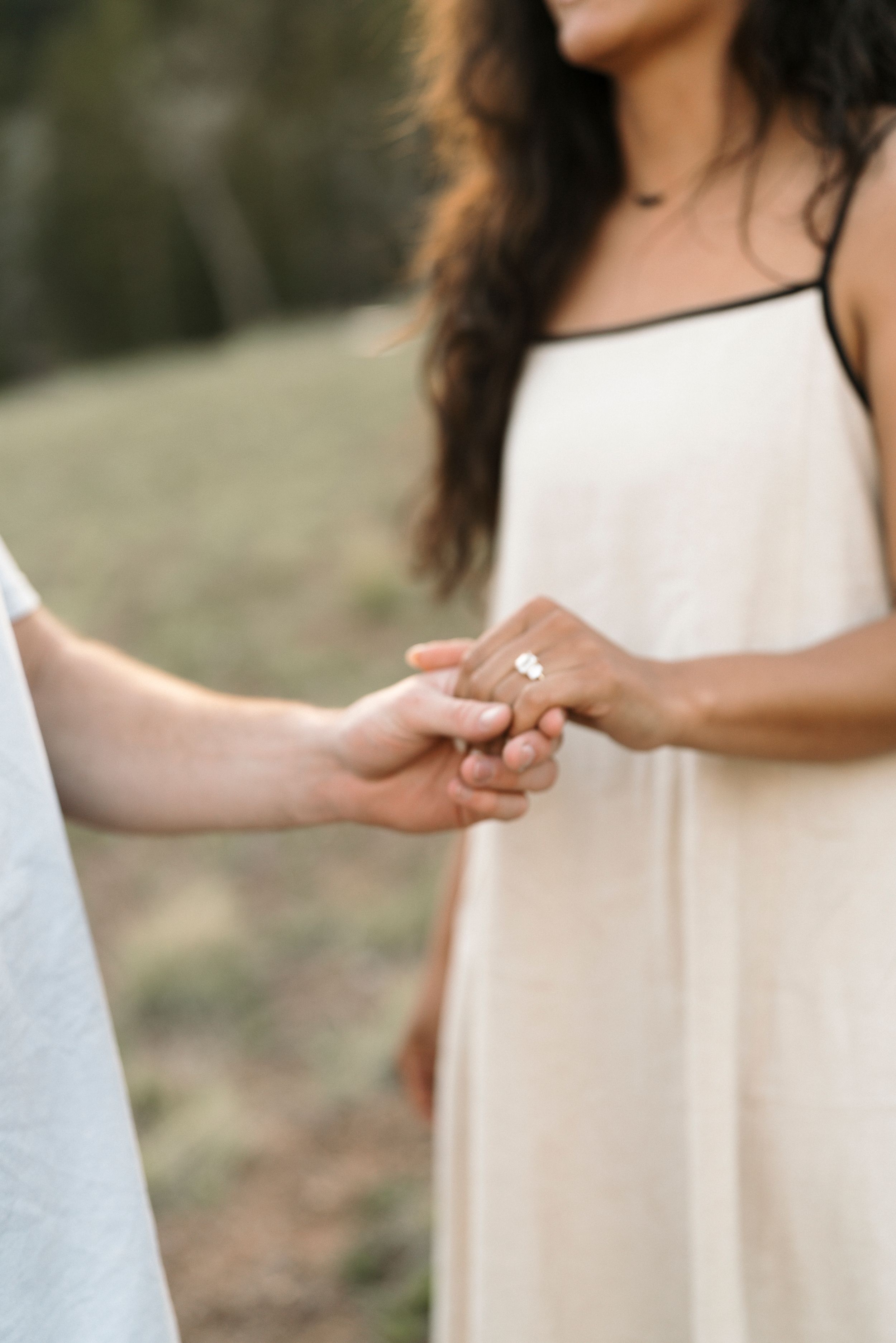 Close-up of two people holding hands with an engagement ring during an outdoor proposal.