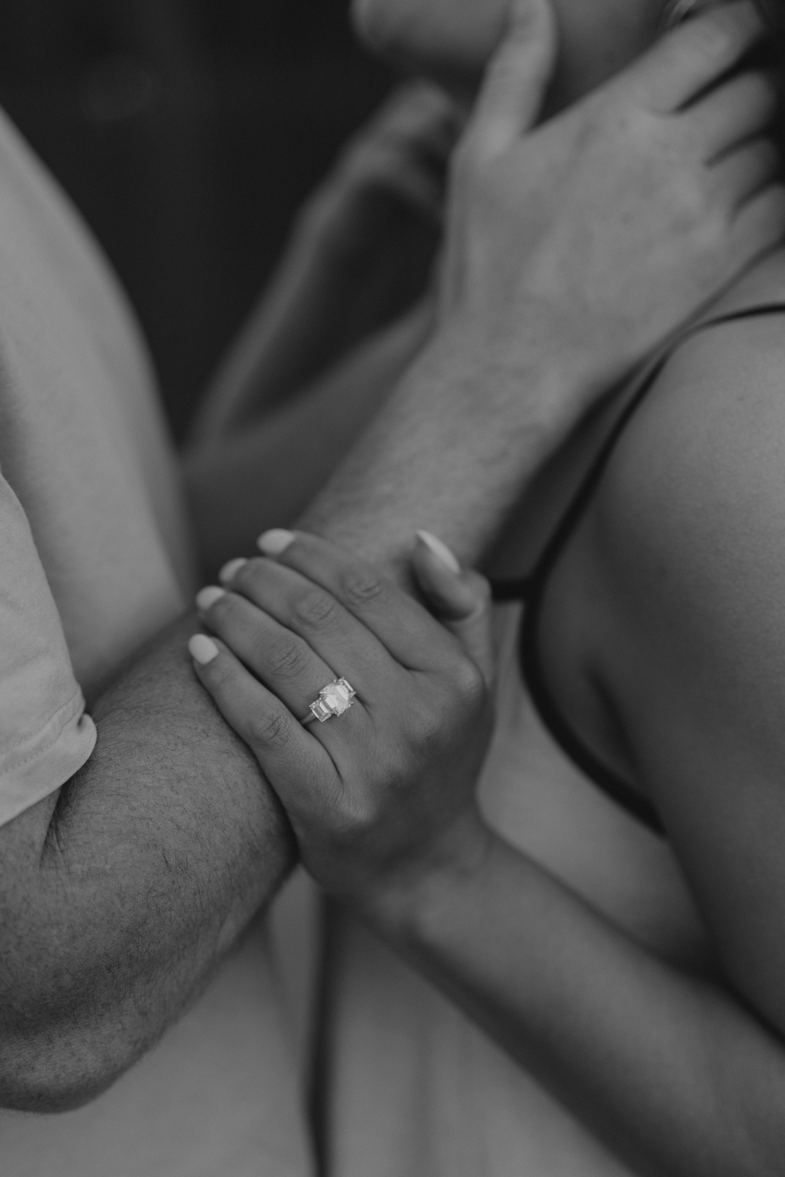 Black and white photo of a couple holding hands, showcasing an elegant engagement ring on the woman's finger.