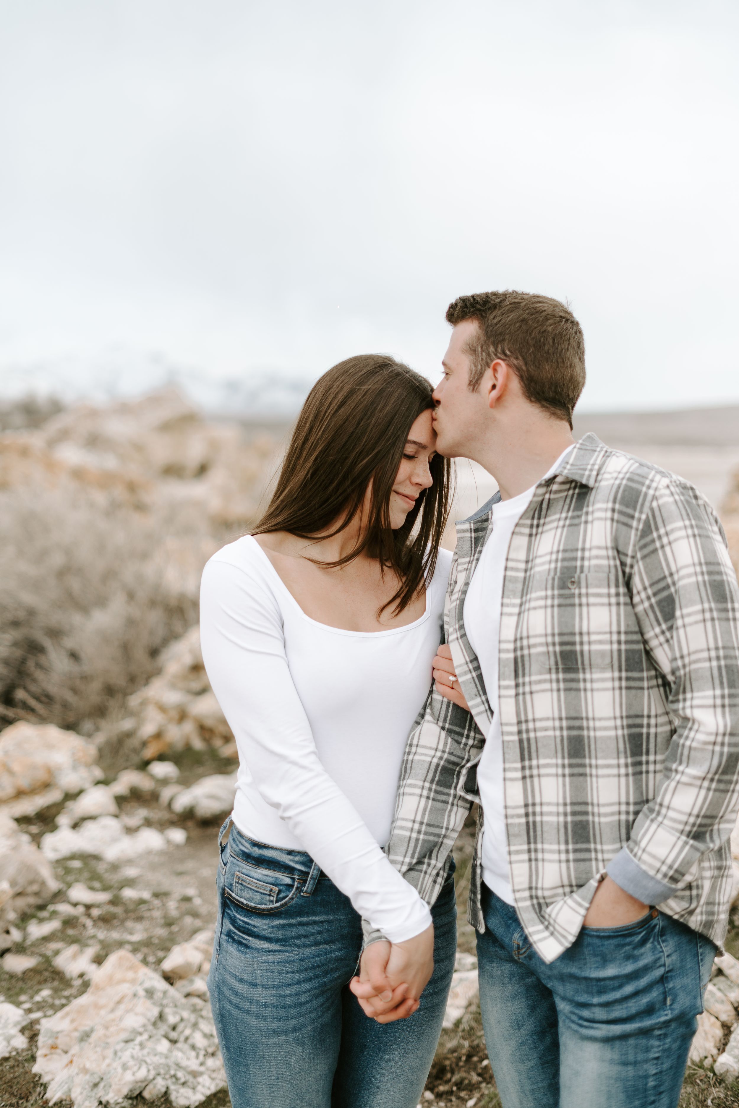 A couple sharing an intimate moment on a rocky hillside in casual attire.
