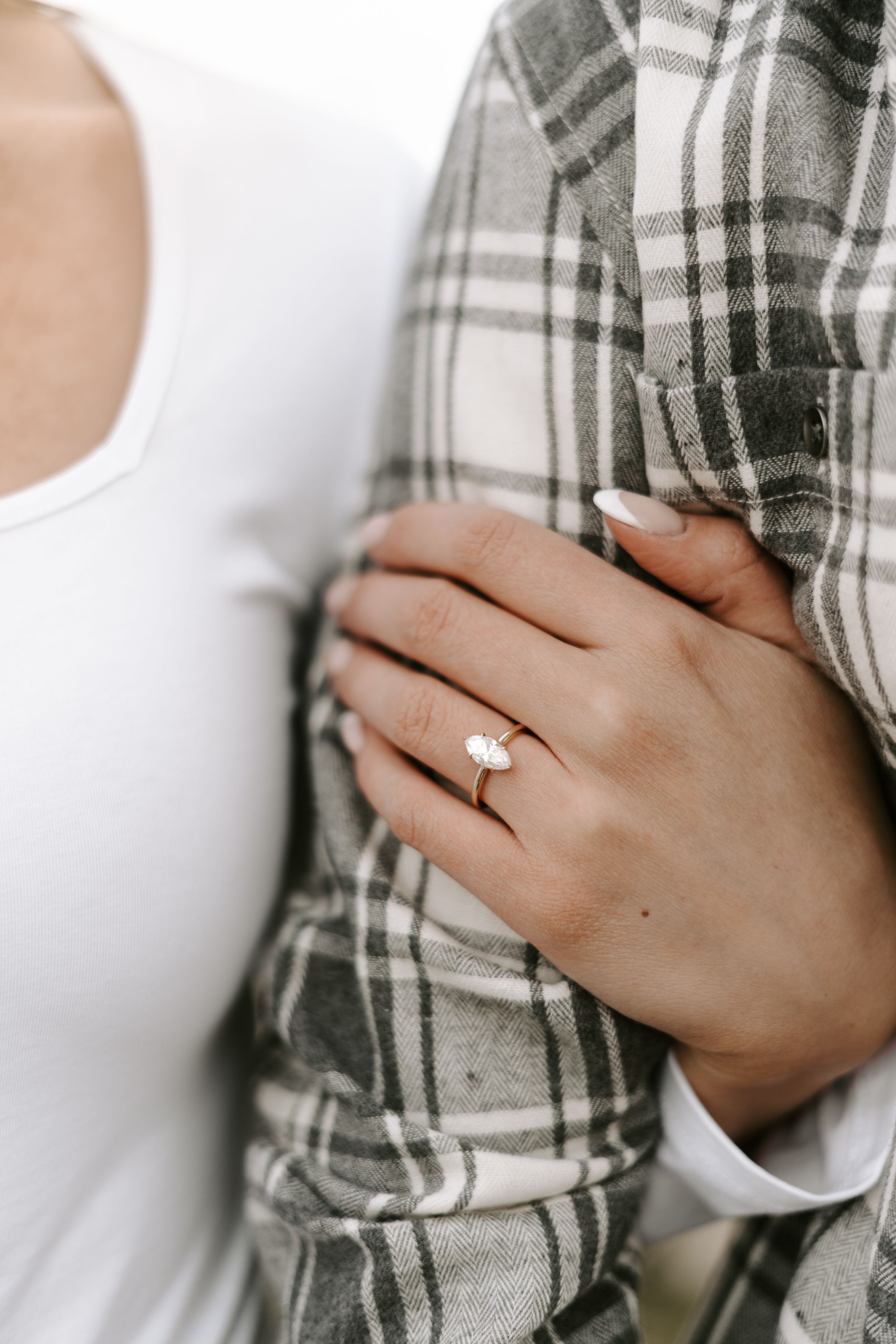 Close-up shot of an engagement ring on a hand against a plaid shirt.
